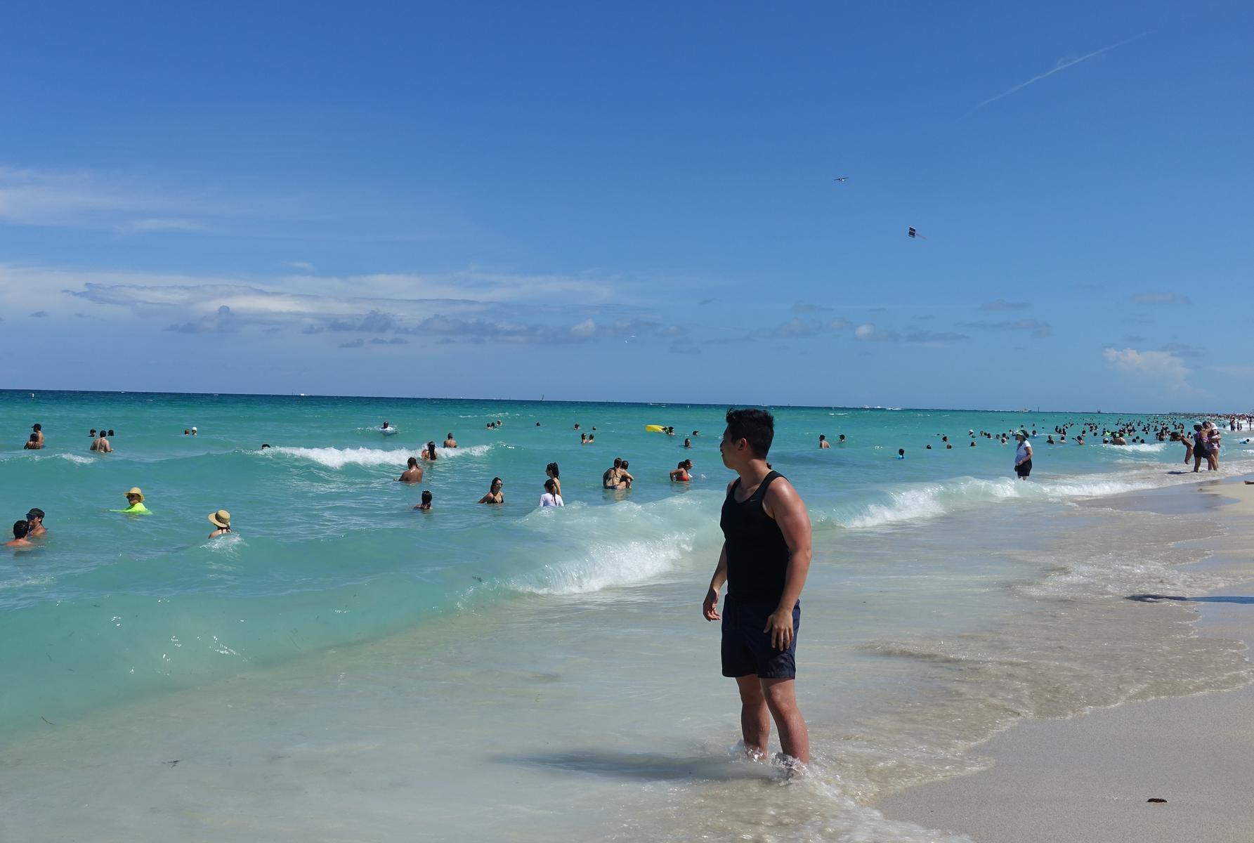 A man stands in the clear turquoise water of a crowded South Beach.