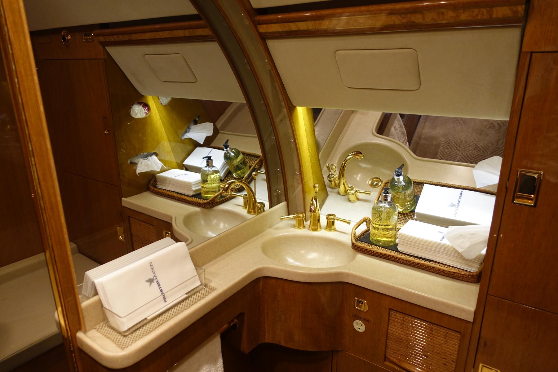 A luxurious private jet lavatory with twin sinks, golden faucets, and branded toiletries.