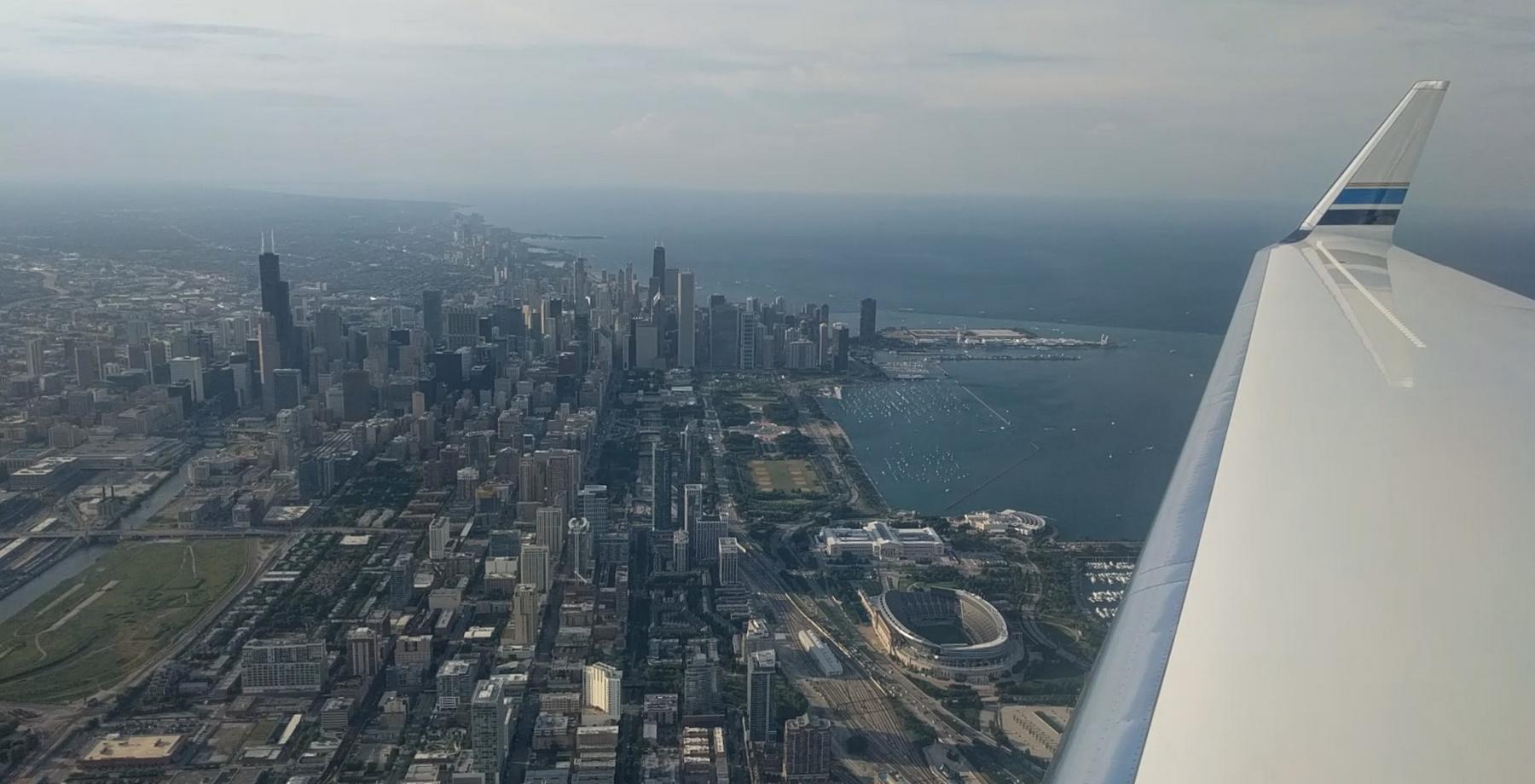 Aerial view of Chicago's skyline, Lake Michigan, and Soldier Field from a private jet wing.