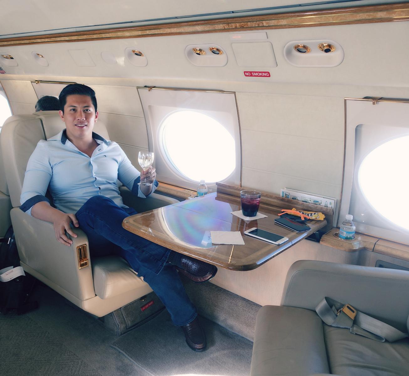 A smiling man holds a glass of wine inside the cabin of a private Gulfstream G5 jet.