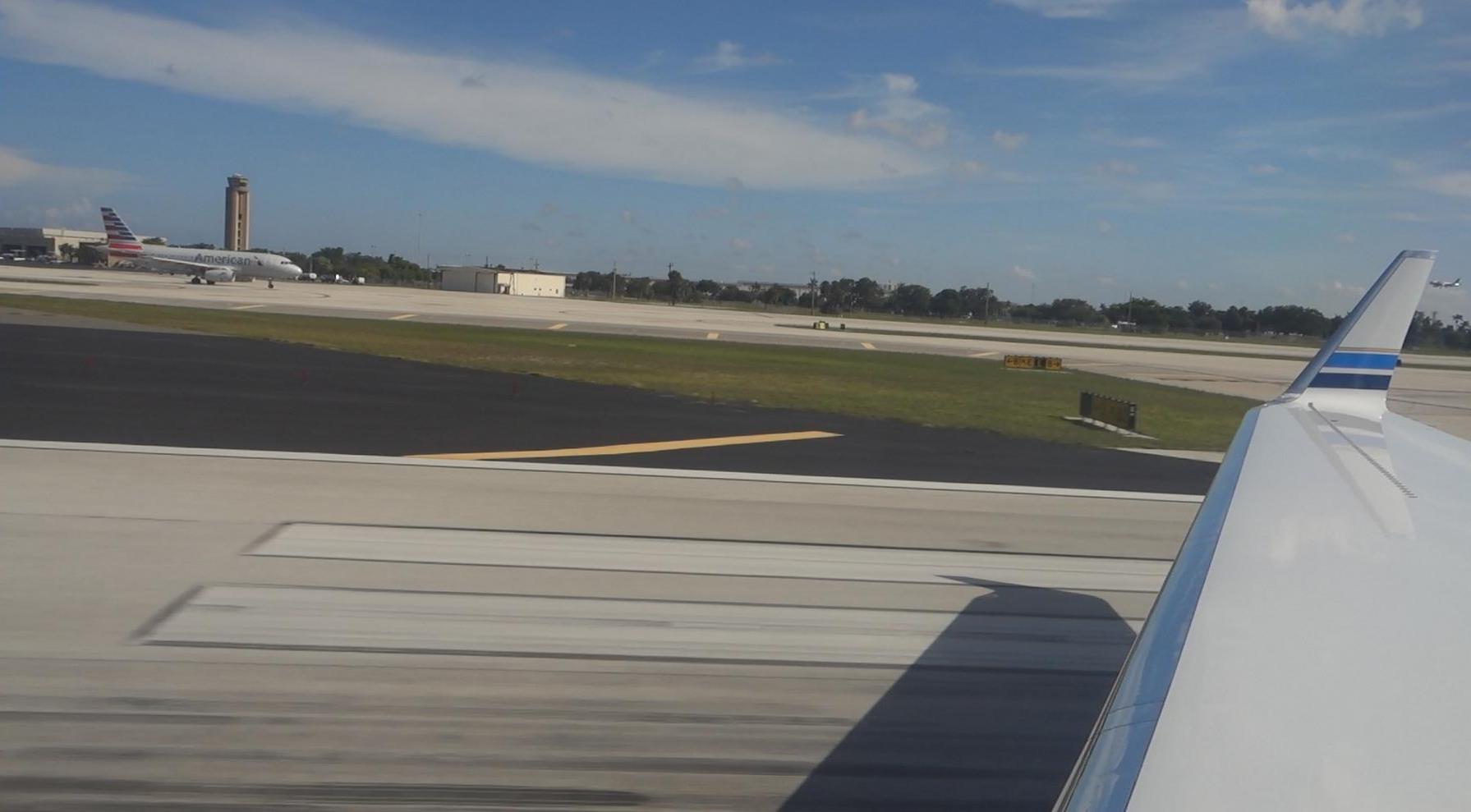 View from a private jet wing on an airport runway, with an American Airlines plane and control tower in the background.