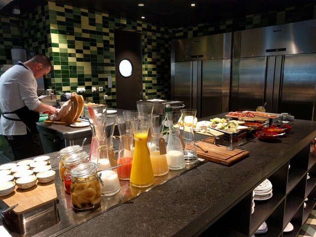 A chef carves ham at a buffet with various drinks and food items.
