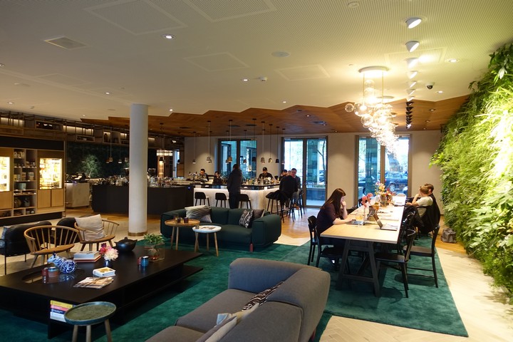 The modern lounge of the Hyatt Regency Amsterdam featuring a bar, various seating areas, and a prominent green living wall.