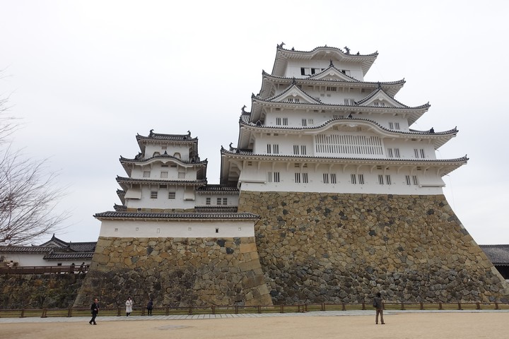 Himeji Castle, a large white multi-tiered Japanese castle, stands on a stone foundation.