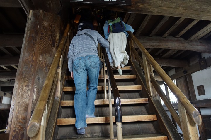 Visitors ascend a steep, rustic wooden staircase within Himeji Castle.