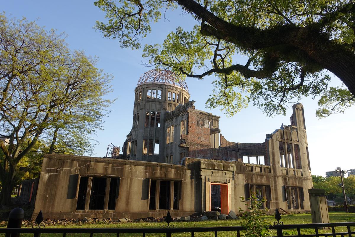 The Atomic Bomb Dome, a partially ruined building, framed by green trees against a clear blue sky in Hiroshima.