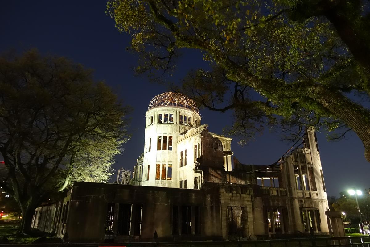 The Hiroshima Atomic Bomb Dome illuminated at night, with trees framing the scene.