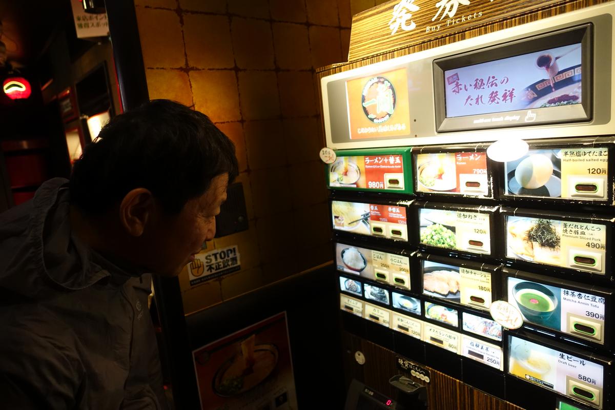 A man looks closely at a Japanese food ticket vending machine displaying various meal options.