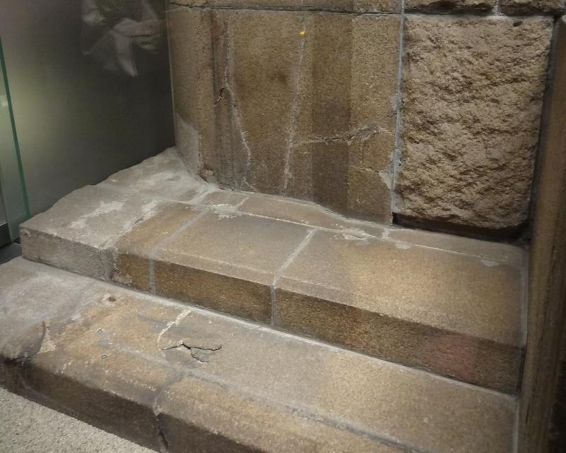 Weathered stone steps with cracks next to a rough stone wall.