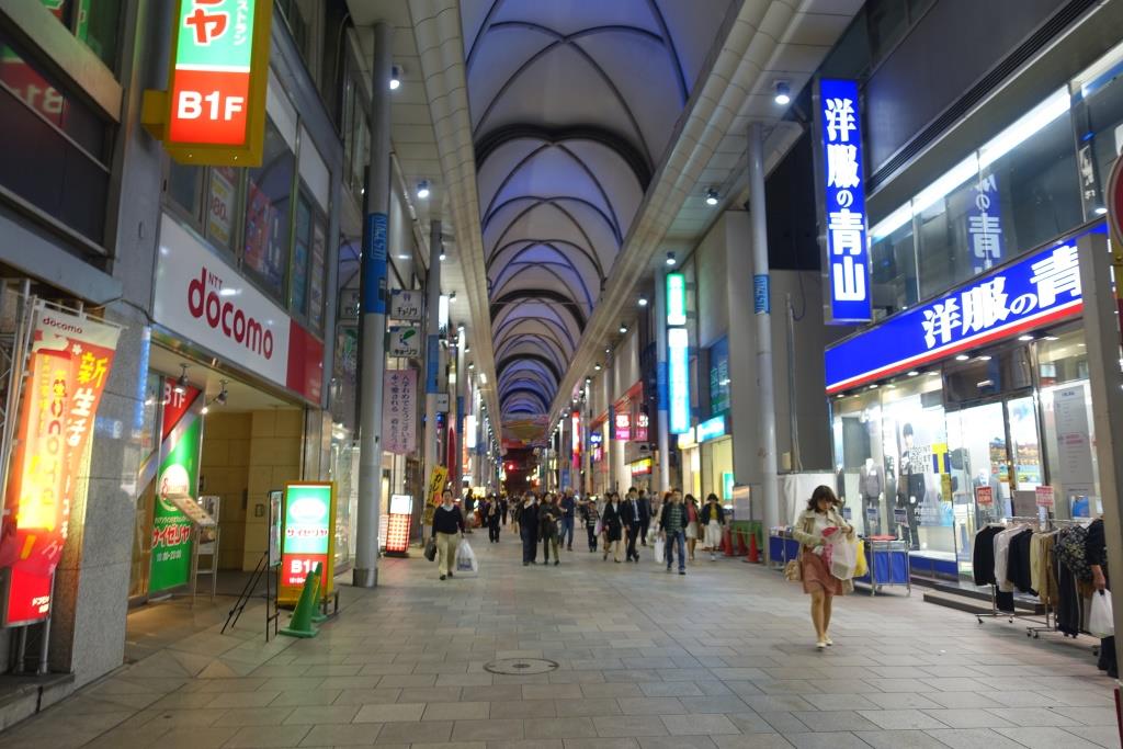 A long, covered shopping arcade lined with brightly lit Japanese shops and pedestrians.