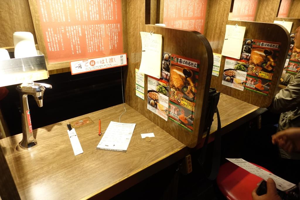 Interior of a Japanese restaurant booth with menus, a water tap, and a person holding a menu.