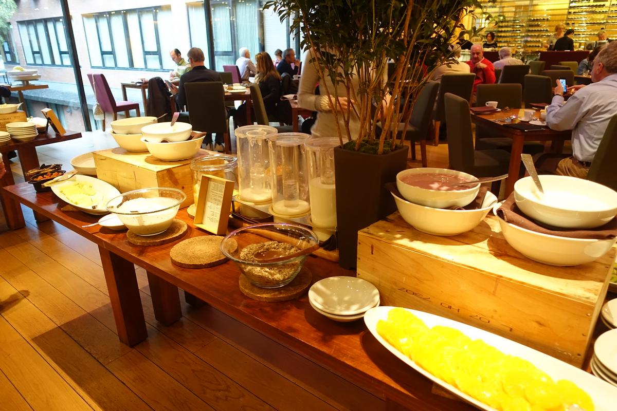 A hotel breakfast buffet with bowls of food and people dining in the background.