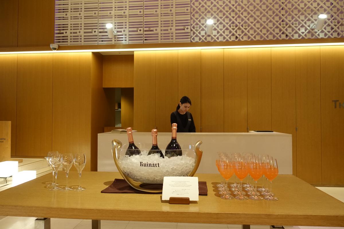 Champagne bottles on ice and glasses of orange drinks on a table in a modern hotel lobby.