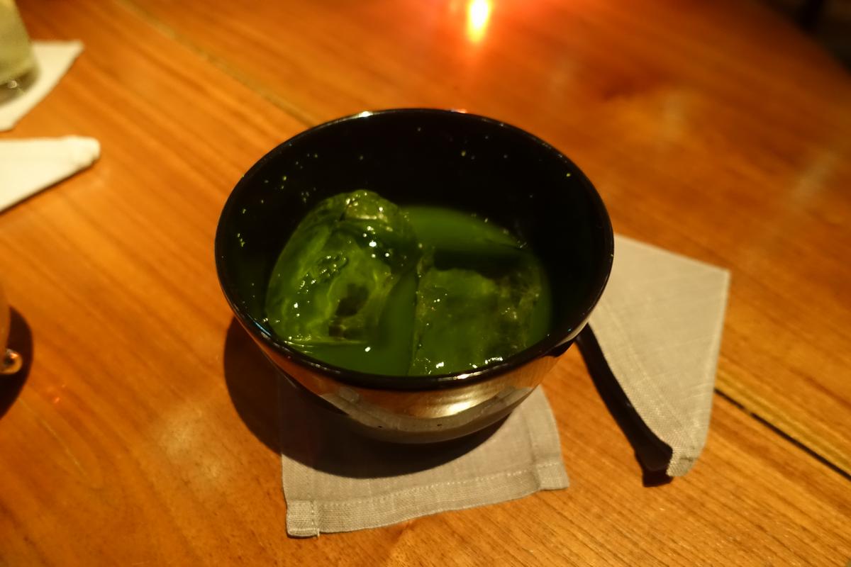 Iced matcha tea in a black bowl on a wooden table.