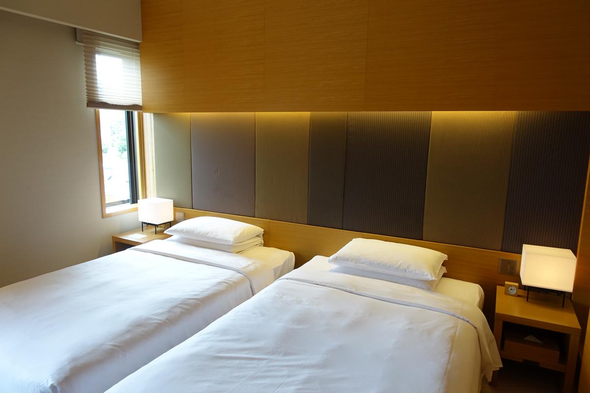Two twin beds in a modern hotel room with a lit paneled headboard and window.