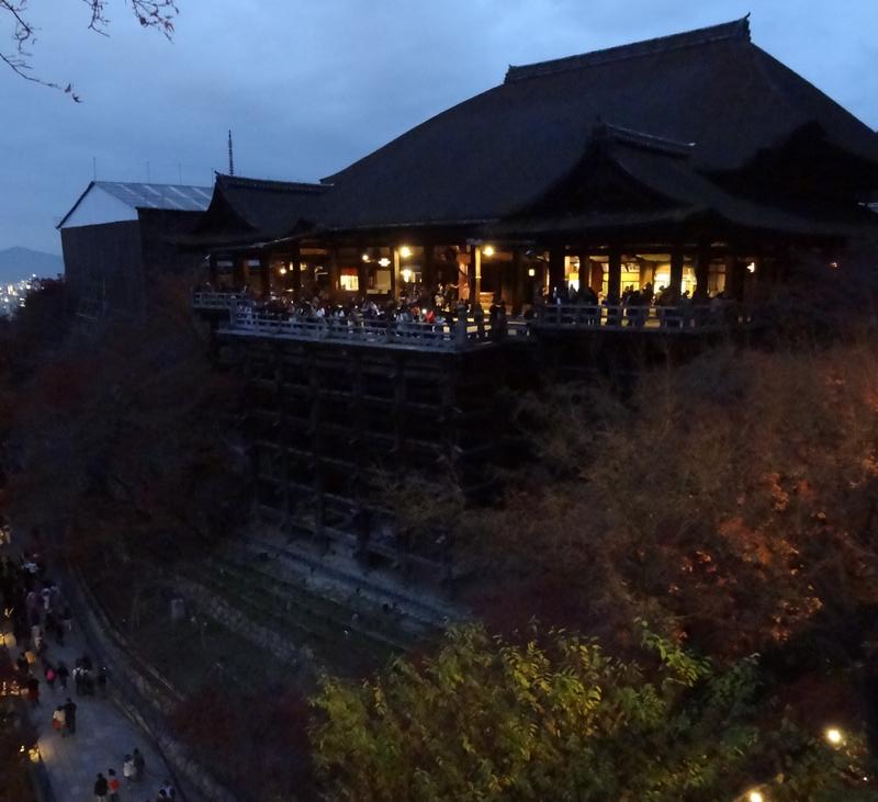 Kiyomizu-dera Temple at dusk, its illuminated wooden platform bustling with visitors.