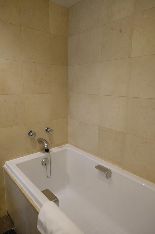A deep white soaking tub with a white towel in a beige tiled bathroom.