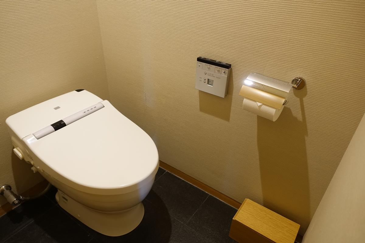 A modern white bidet toilet with a wall-mounted control panel in a beige bathroom.