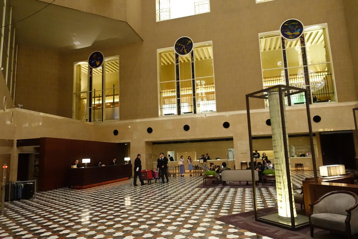 The grand atrium lobby of the Hyatt Regency Tokyo, with a patterned floor, reception desk, and a tall illuminated sculpture.