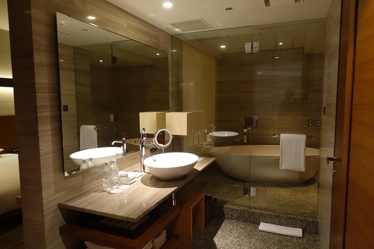 A modern hotel bathroom featuring a double vanity with vessel sinks and a large soaking tub behind a glass partition.