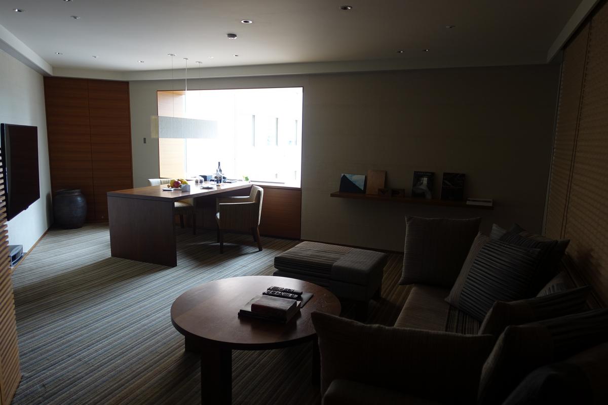 A modern hotel suite with a bright dining area and a dimly lit living room.