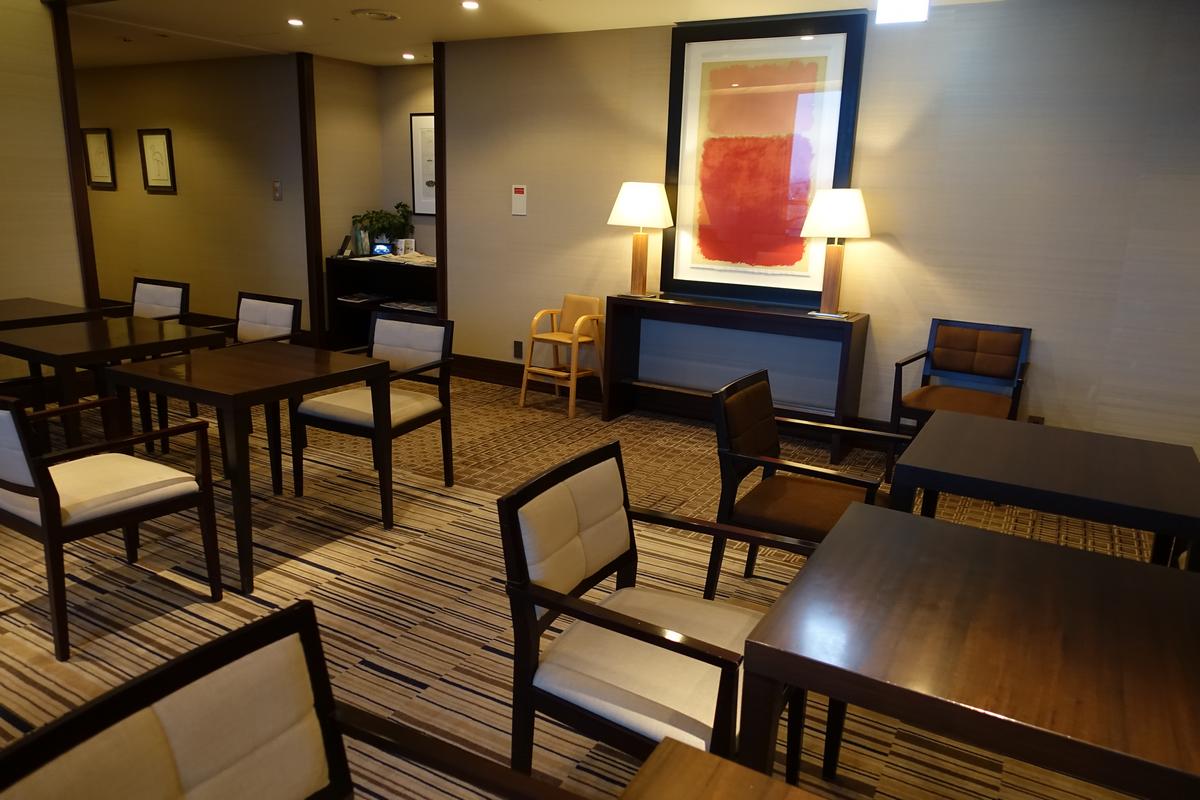 A hotel lounge with multiple dark wood tables, chairs, and a large abstract painting on the wall.