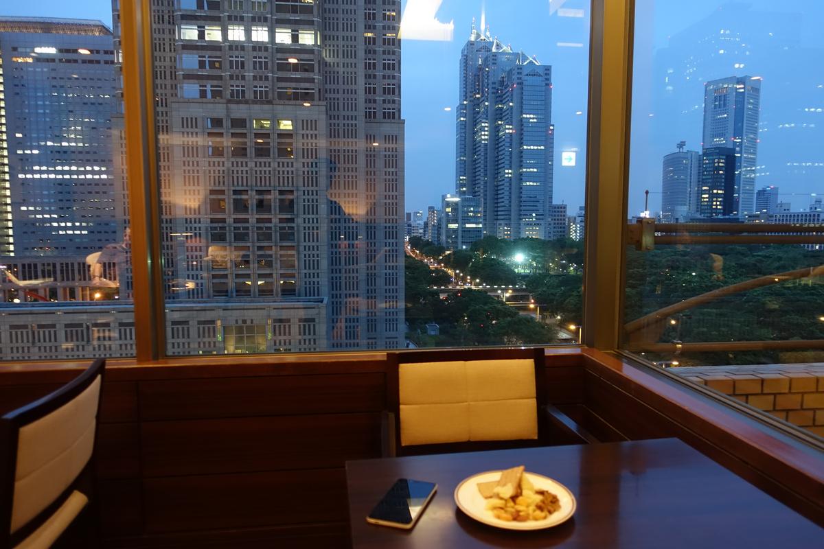 A plate of snacks and a phone on a table with a nighttime city view of tall buildings and a park.