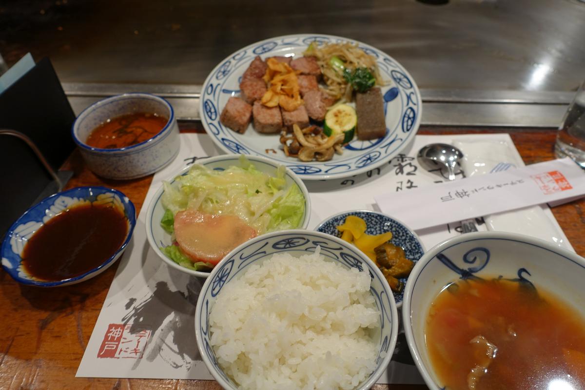 A full set meal featuring cooked Kobe beef, rice, salad, soup, and various sides on a restaurant table.
