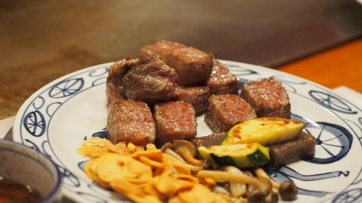 Plate of seared Kobe beef cubes with vegetables and crispy garlic.
