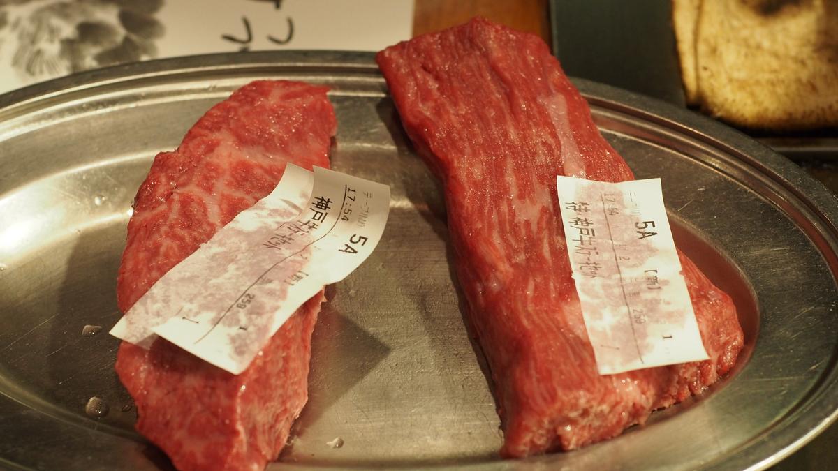 Two raw, marbled Kobe beef pieces with labels on a silver platter.
