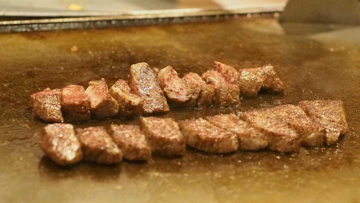 Kobe beef pieces searing on a teppanyaki grill.
