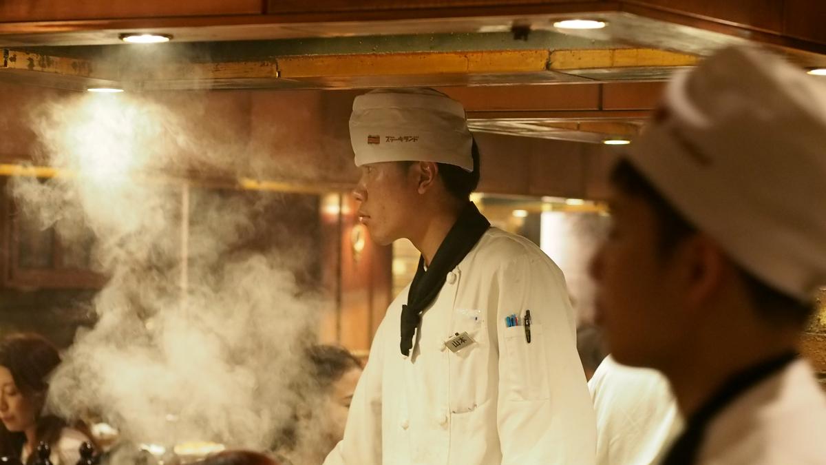 A chef cooks on a grill, surrounded by steam, at a teppanyaki steak restaurant.