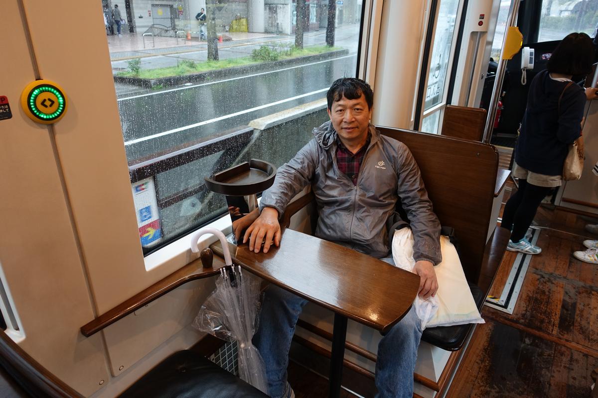 A man sits inside a train next to a window with rain falling outside.