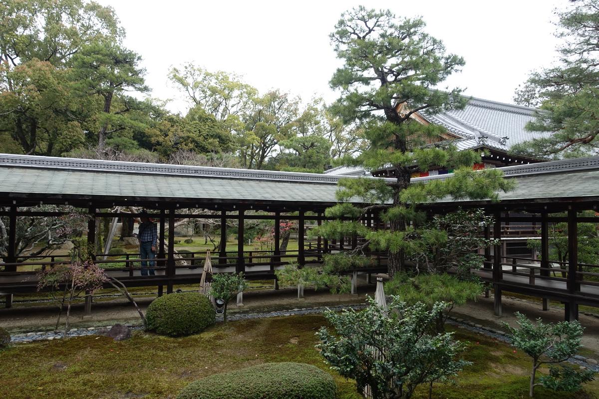 A person walks along covered wooden walkways through a lush Japanese temple garden.