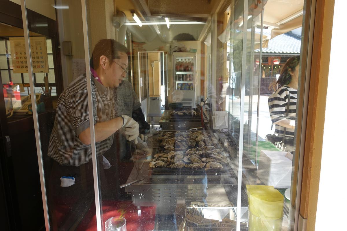A vendor grills rows of oysters behind a glass window.