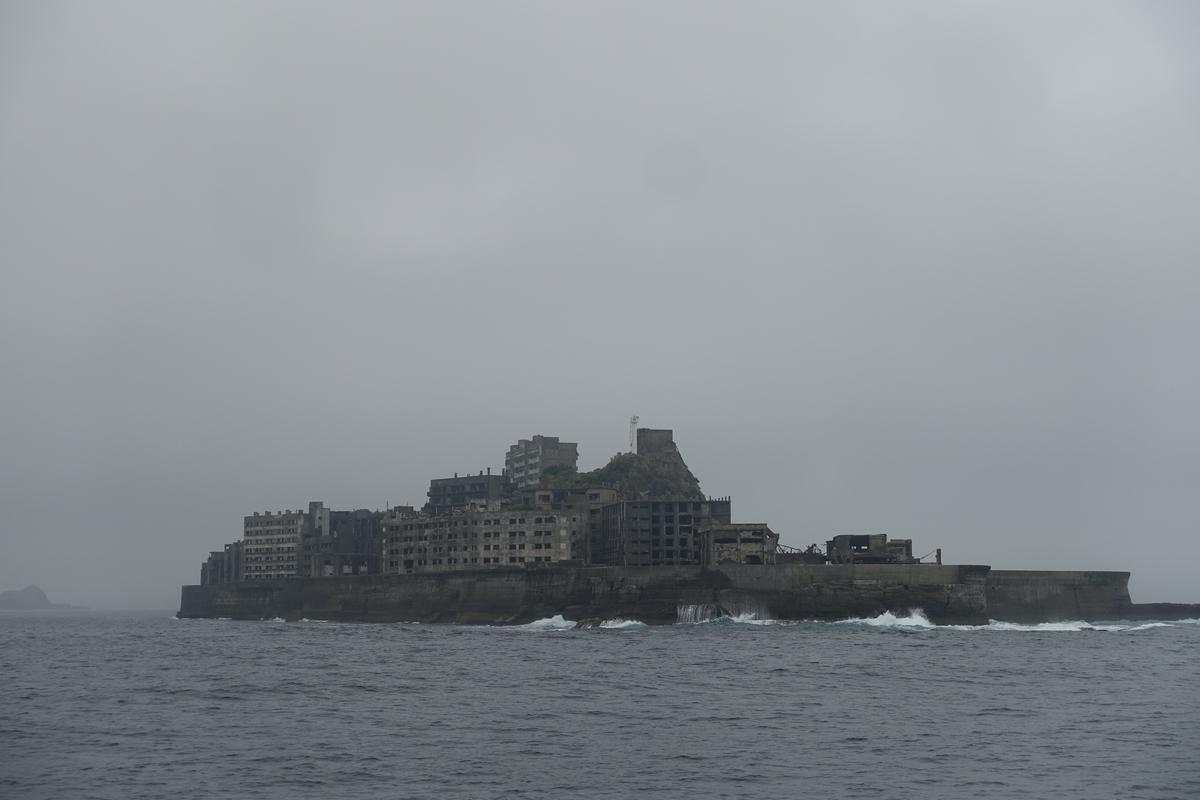 Hashima Island (Battleship Island), covered with decaying concrete buildings, rises from the sea under an overcast sky.