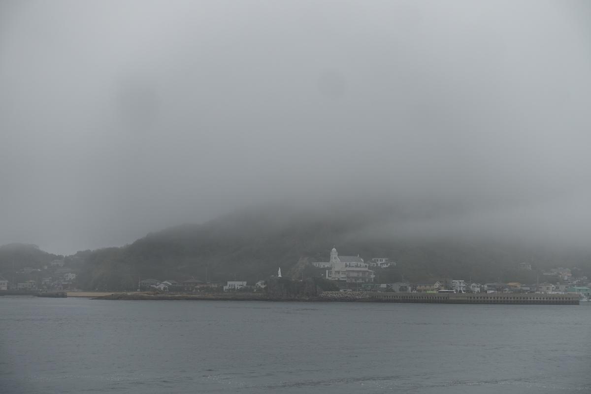 A misty view of a coastal town with a white church on a hill, shrouded in dense fog.