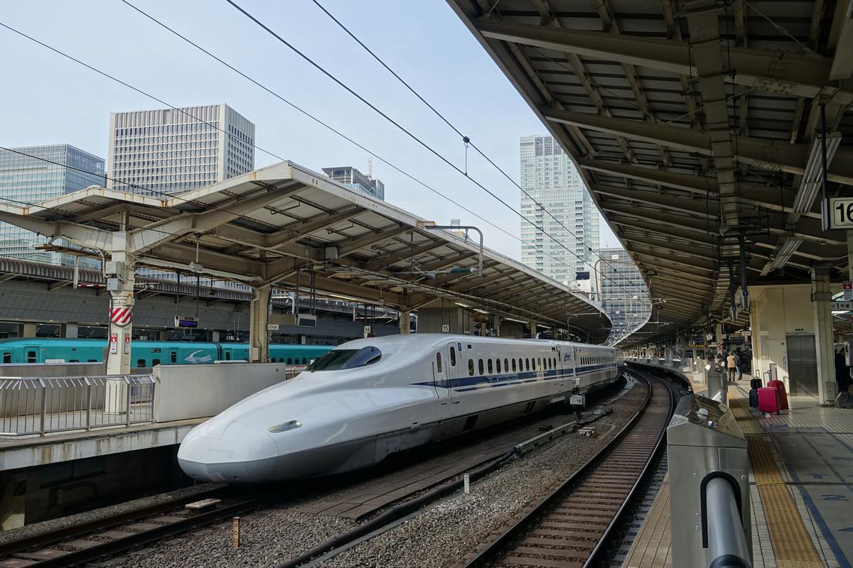 A white Shinkansen bullet train sits on tracks at a station platform.