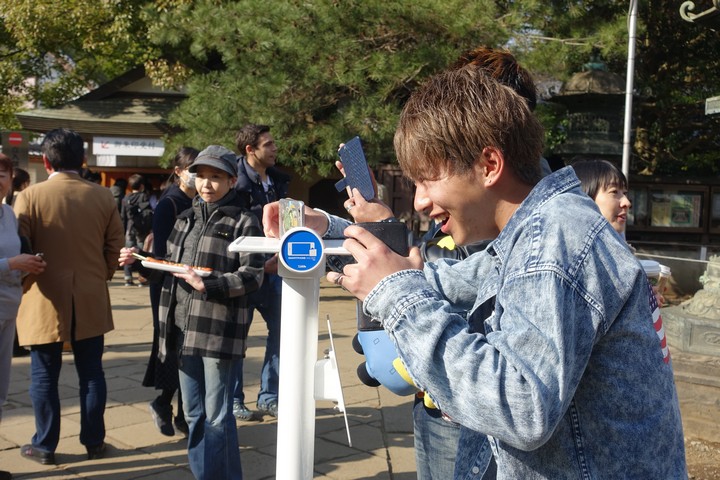 A smiling young man in a denim jacket uses an outdoor charging station.