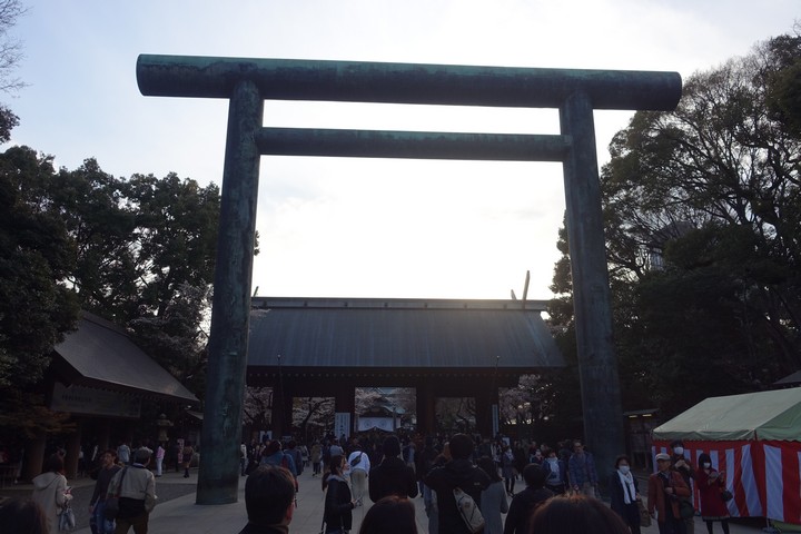 Large bronze torii gate at Yasukuni Shrine with many people below.