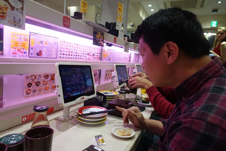 A man uses a tablet to order food at a conveyor belt sushi restaurant.