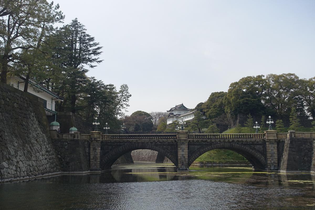 A stone arched bridge crosses the Imperial Moat, with traditional palace-like buildings visible among trees on the far bank.