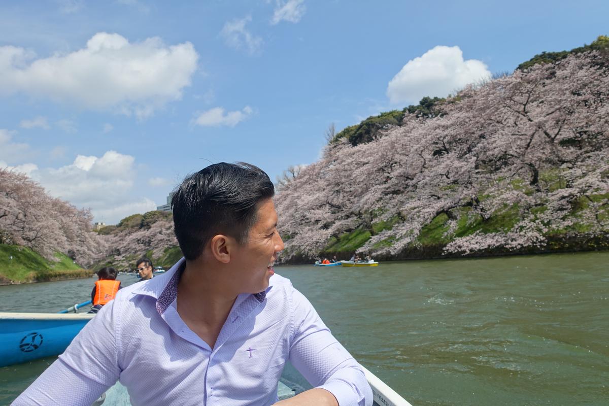 A man smiles from a boat surrounded by cherry blossoms in full bloom on the Chidorigafuchi Imperial Moat.