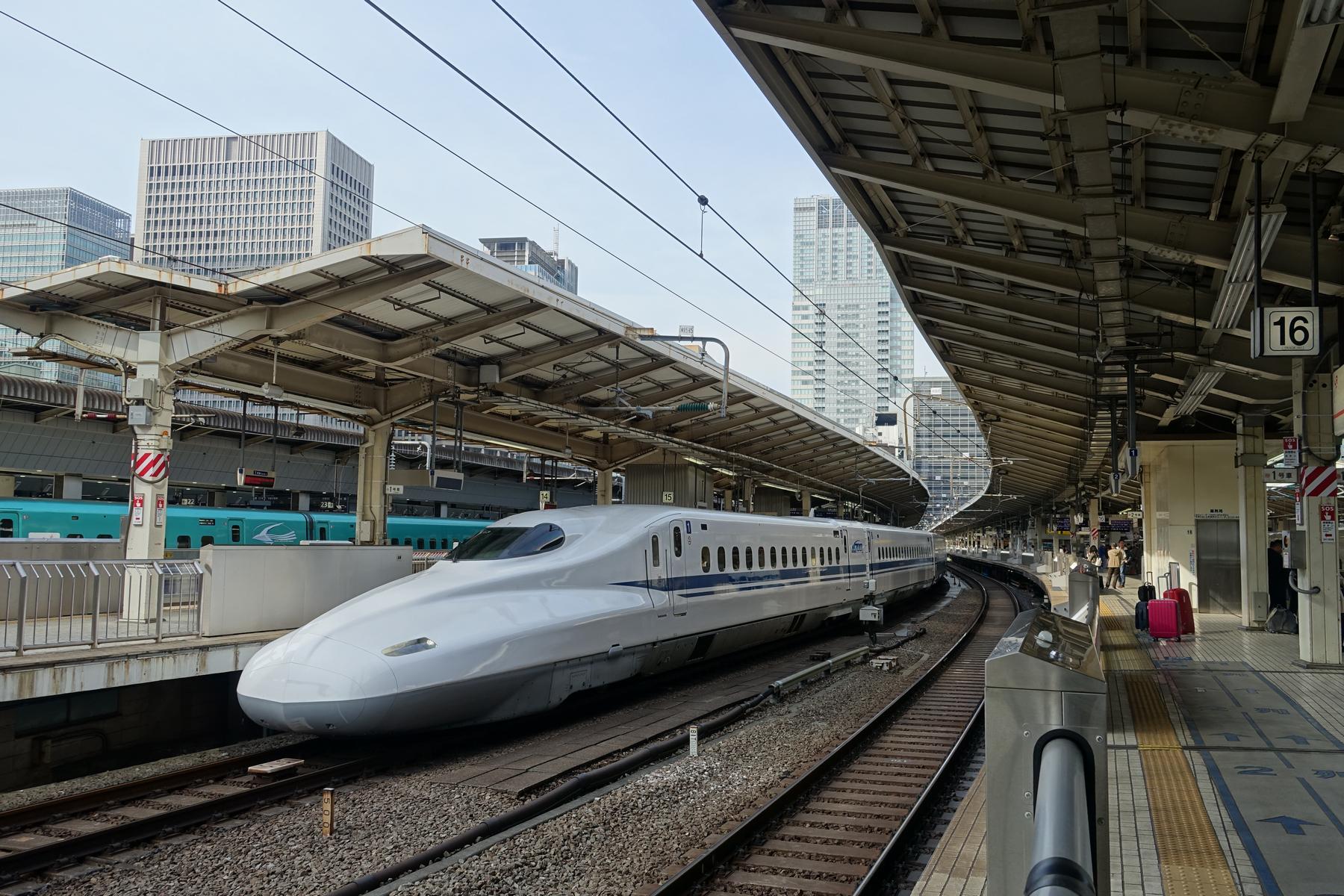 A white Shinkansen bullet train waits at a Japanese station platform.