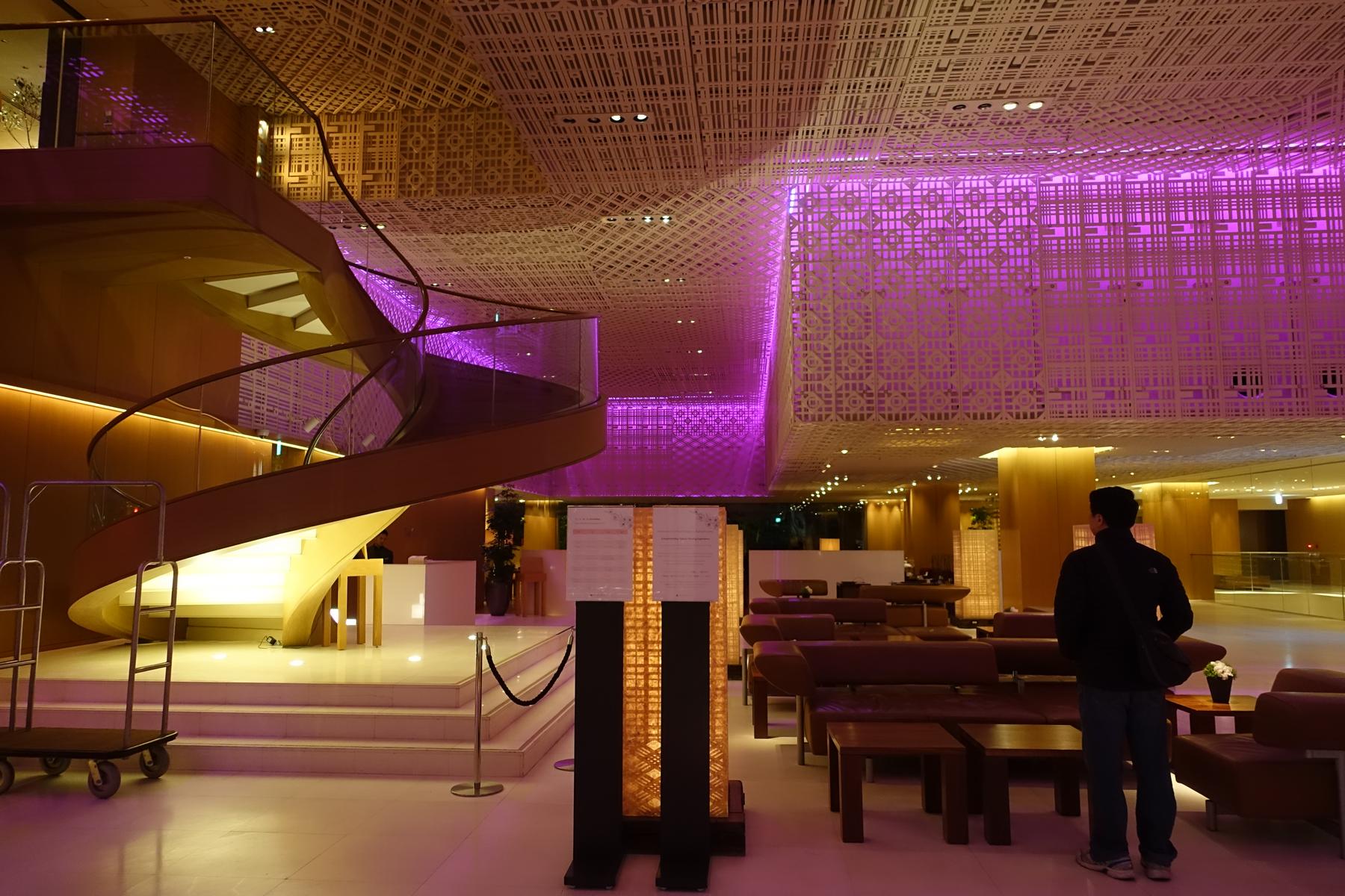 A modern hotel lobby with a spiral staircase, geometric ceiling patterns, and dramatic purple lighting.