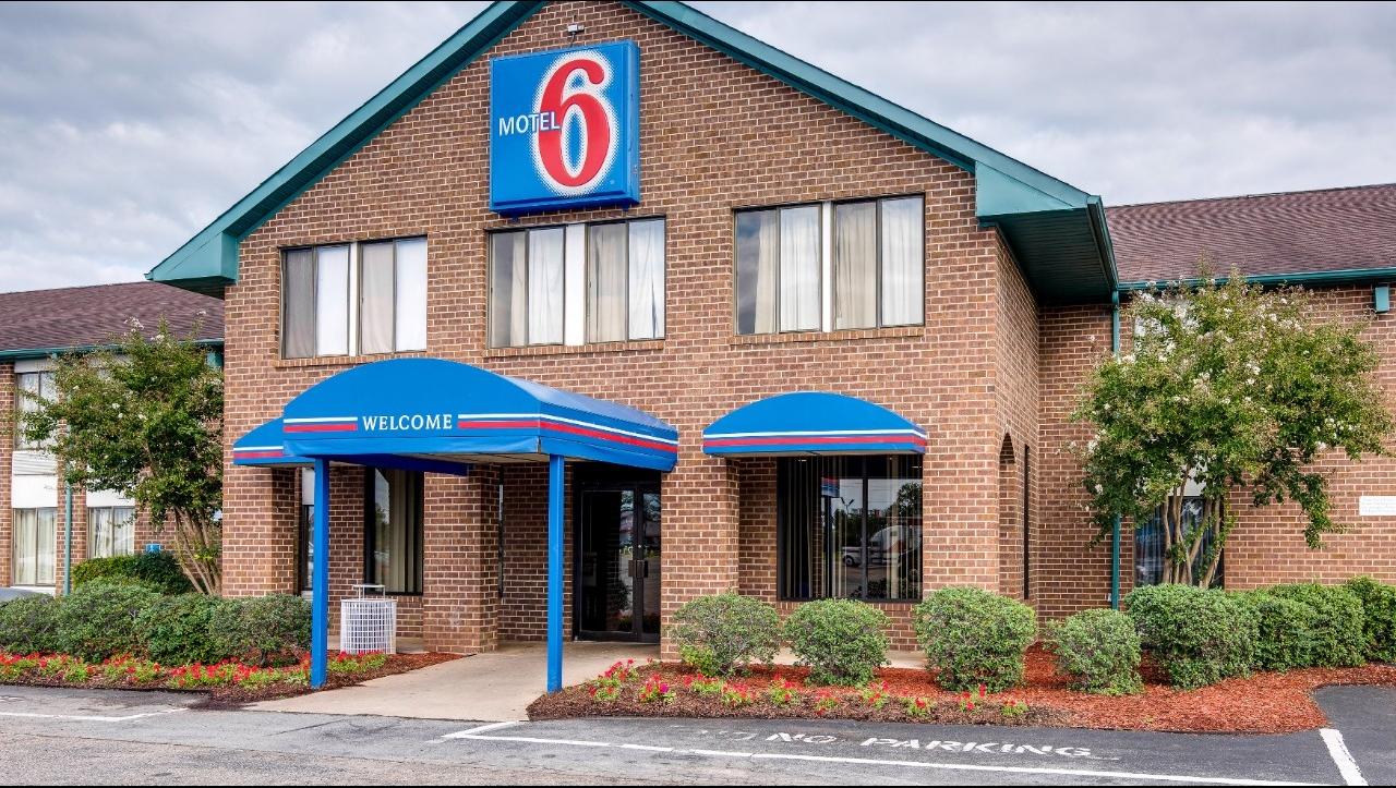 A brick Motel 6 building with its sign prominently displayed and blue welcome awnings.