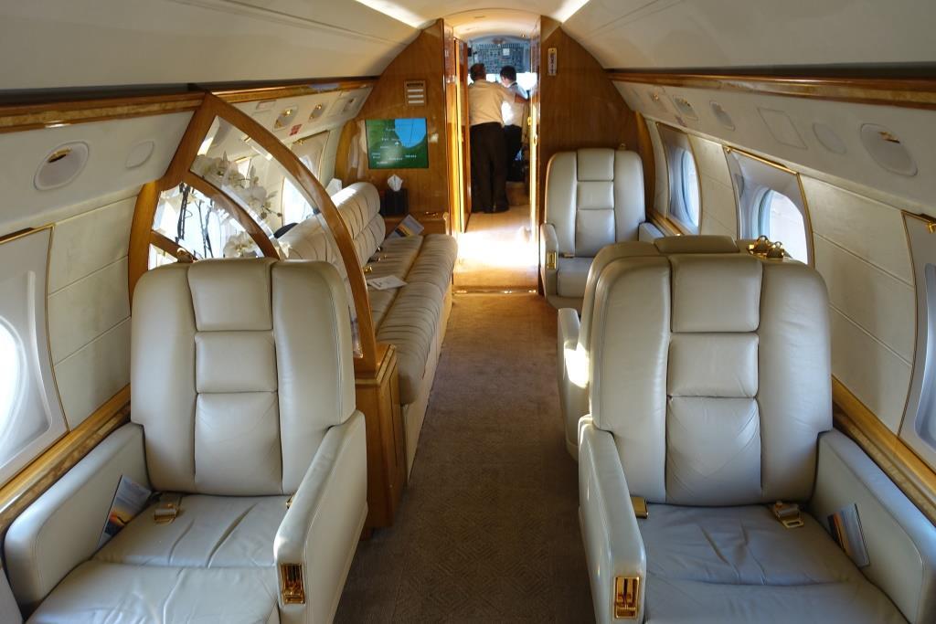 The luxurious interior of a private jet featuring cream leather seats and two crew members visible at the rear.