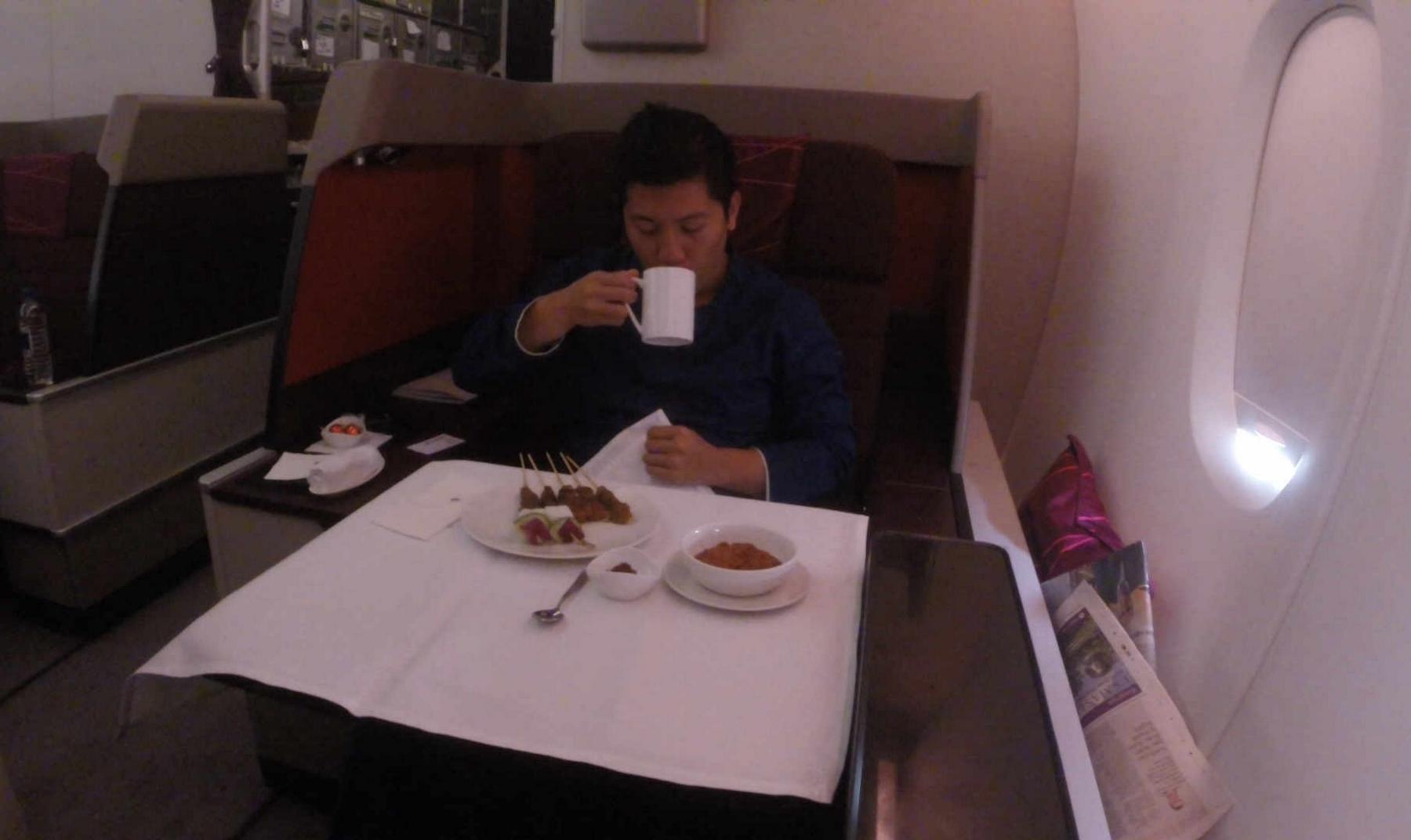 A man sips from a mug while dining on satay in a Malaysia Airlines First Class cabin.
