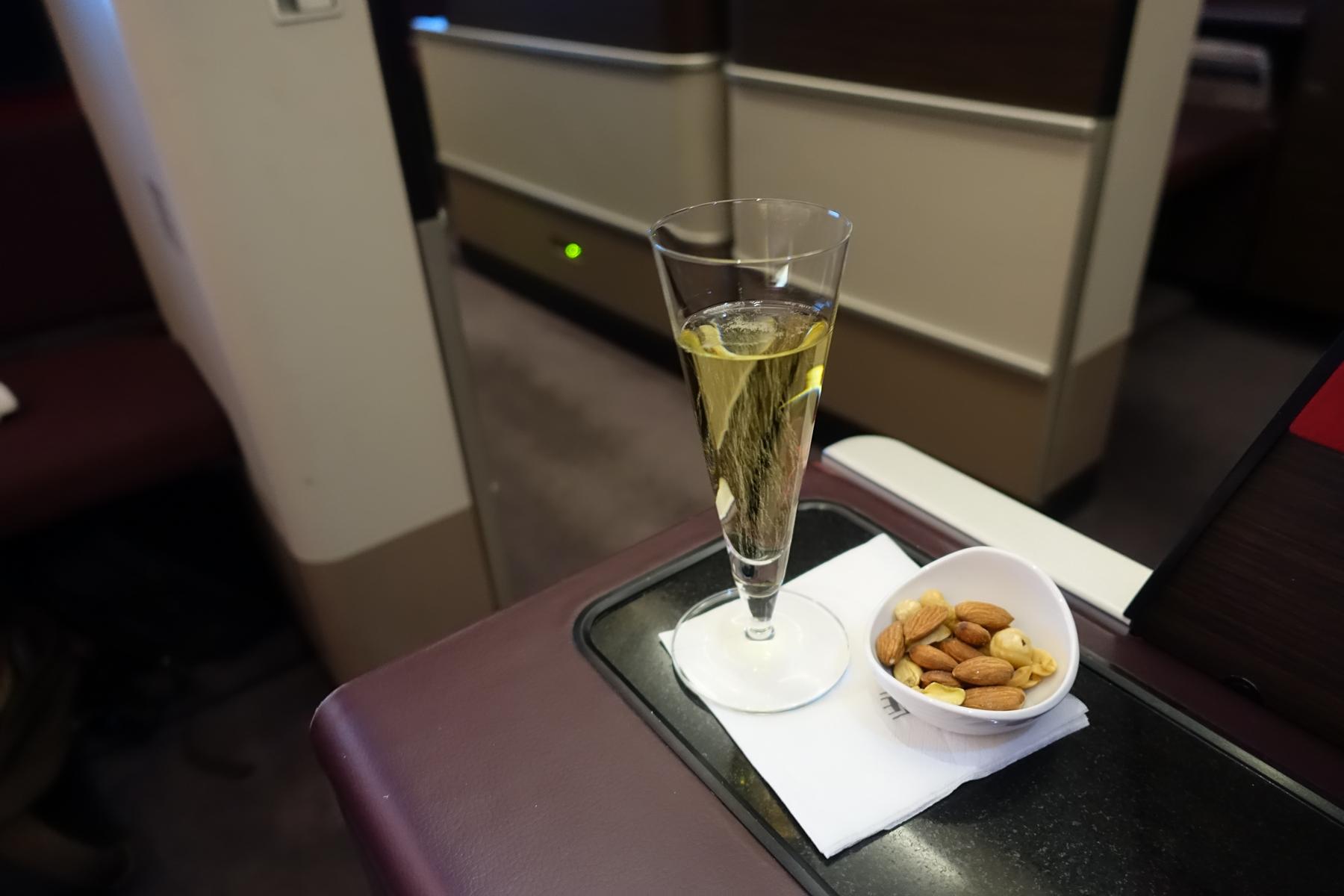 A glass of champagne and a bowl of nuts on a tray in a first class airplane cabin.