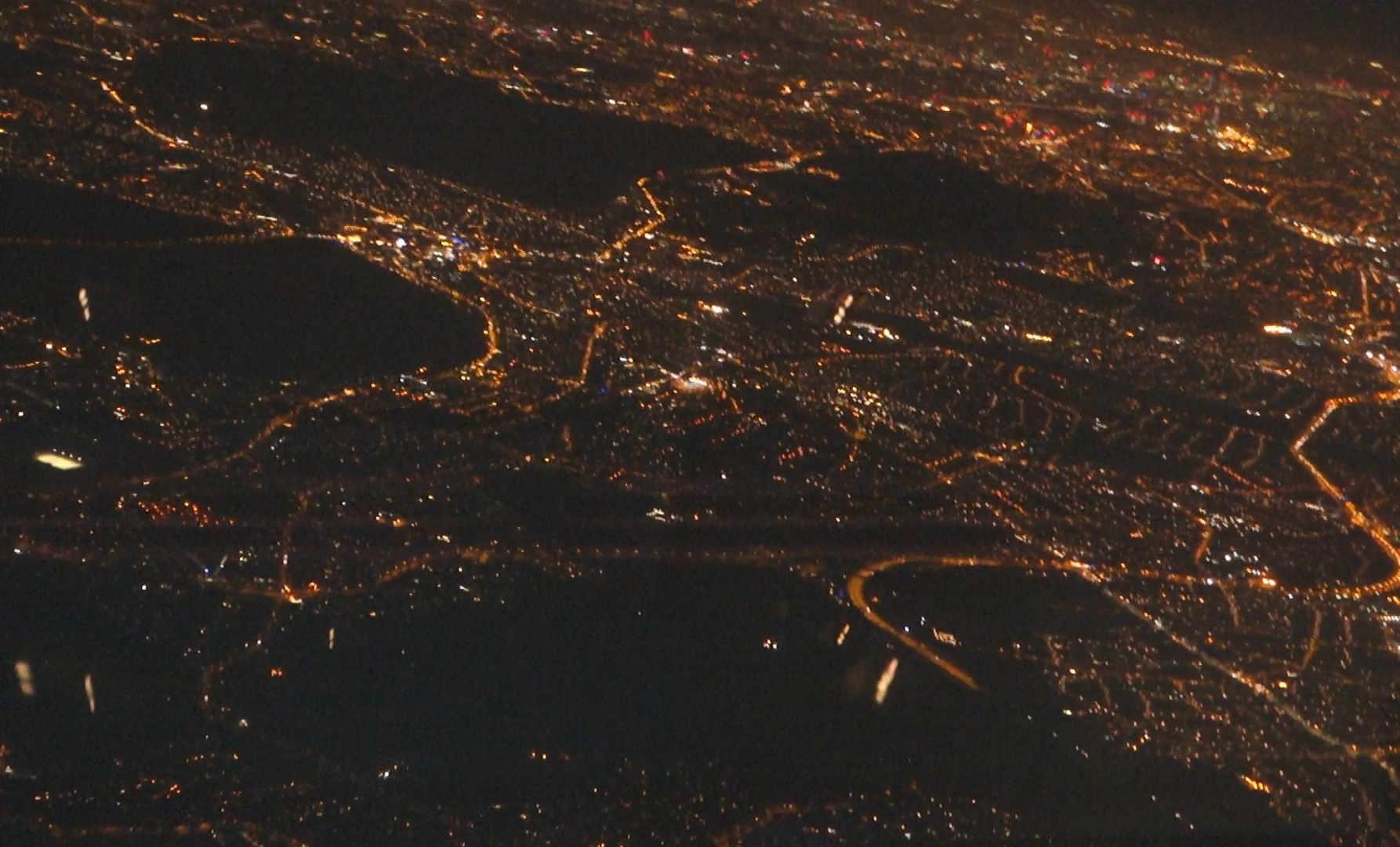 Aerial view of a city at night, with a vast network of glowing lights outlining roads and buildings.